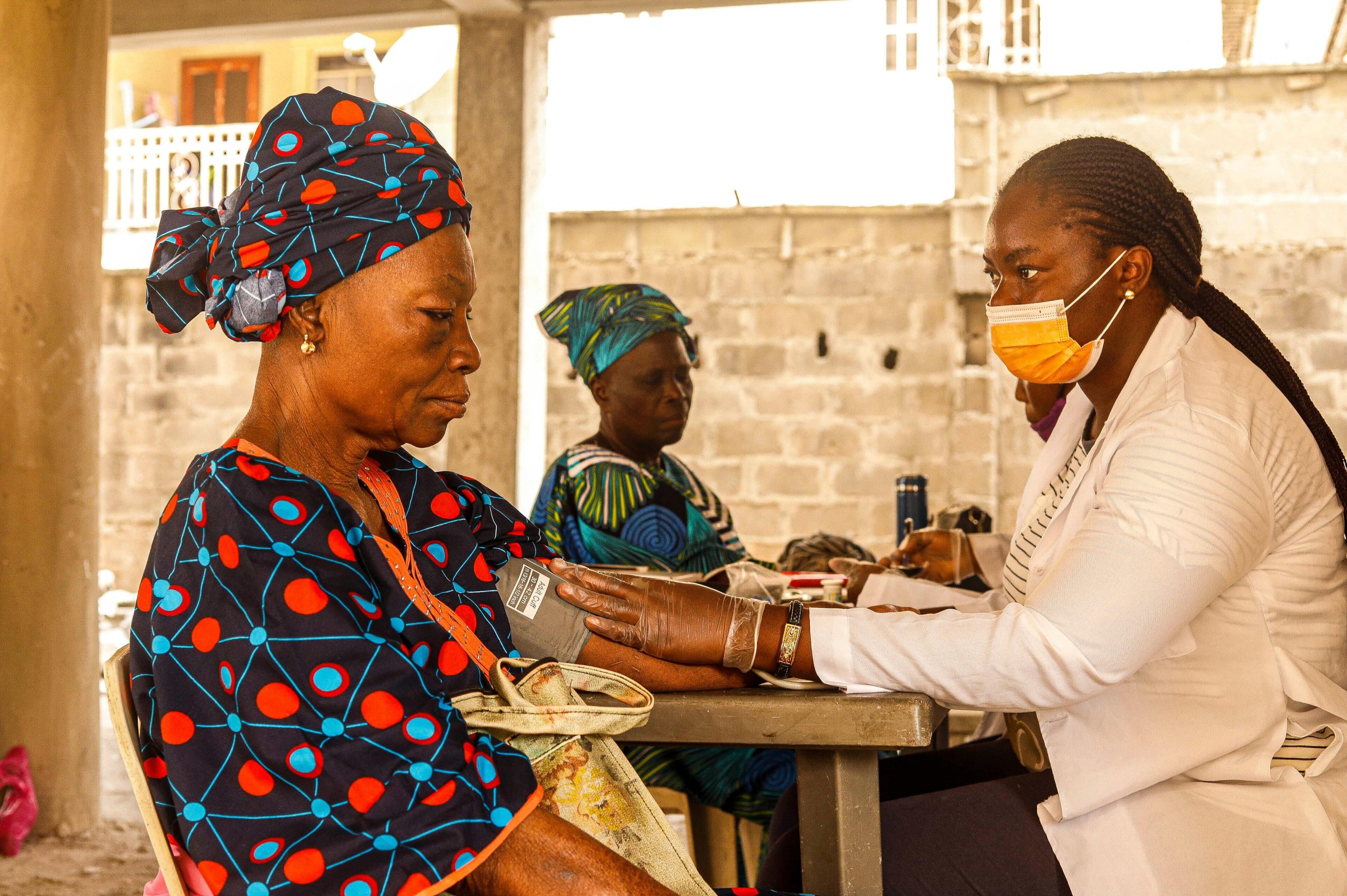 A healthcare worker checks blood pressure of an elderly woman in a rural clinic setting.