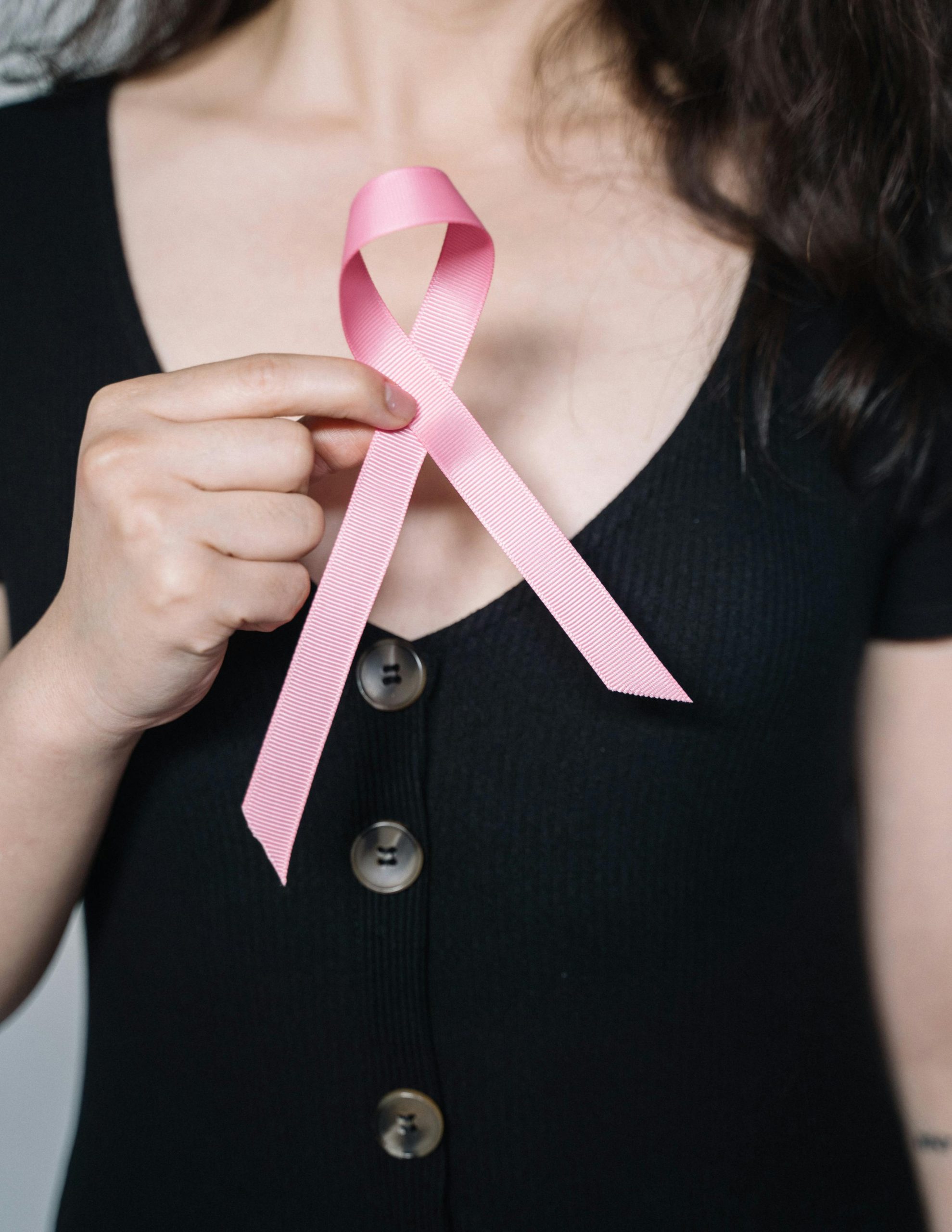 A woman holds a pink ribbon symbolizing breast cancer awareness, promoting health advocacy.