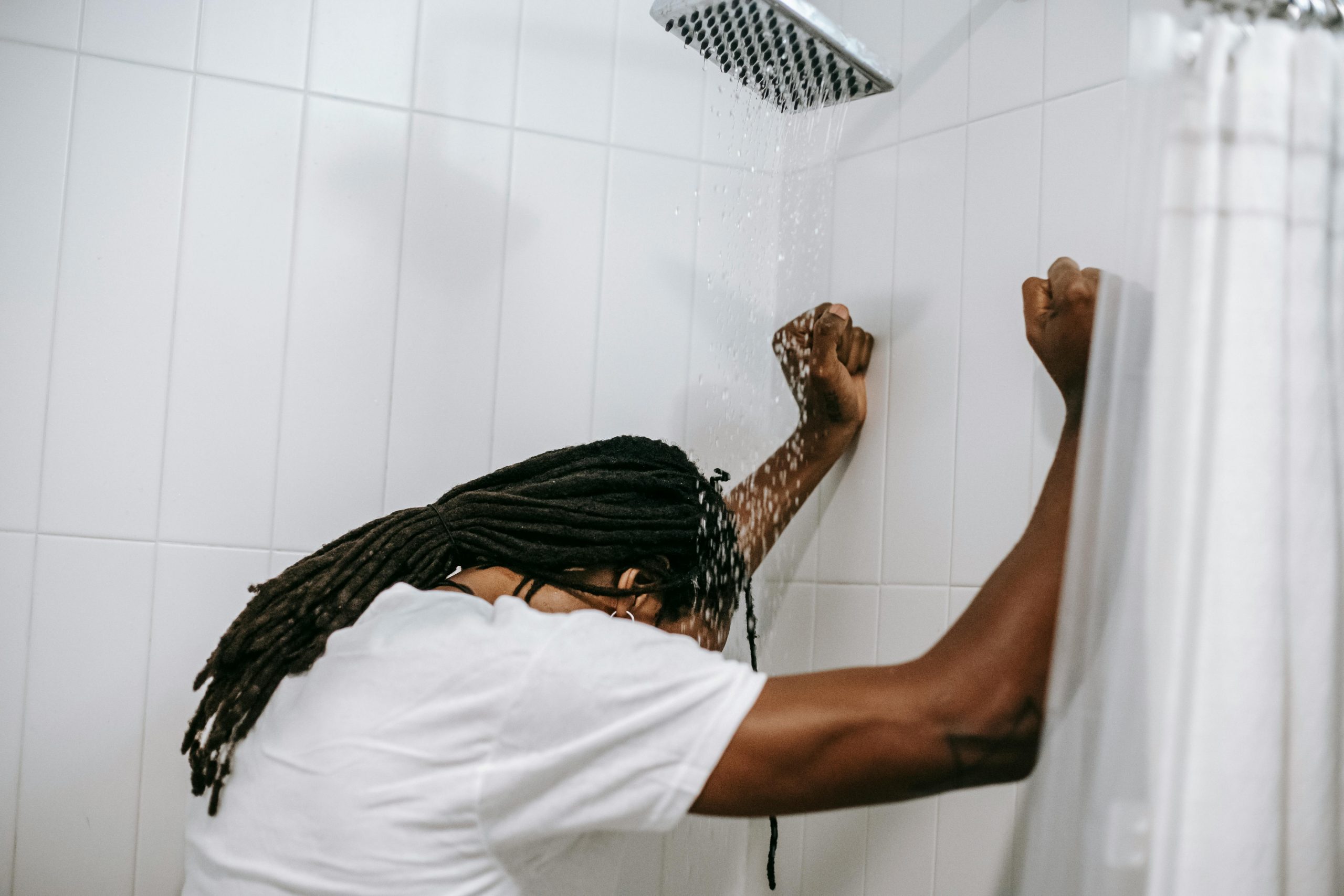 A man stands under a shower with head bowed, depicting contemplation and reflection.