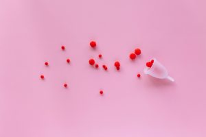 Menstrual cup with red elements on pink background symbolizing menstruation and femininity.
