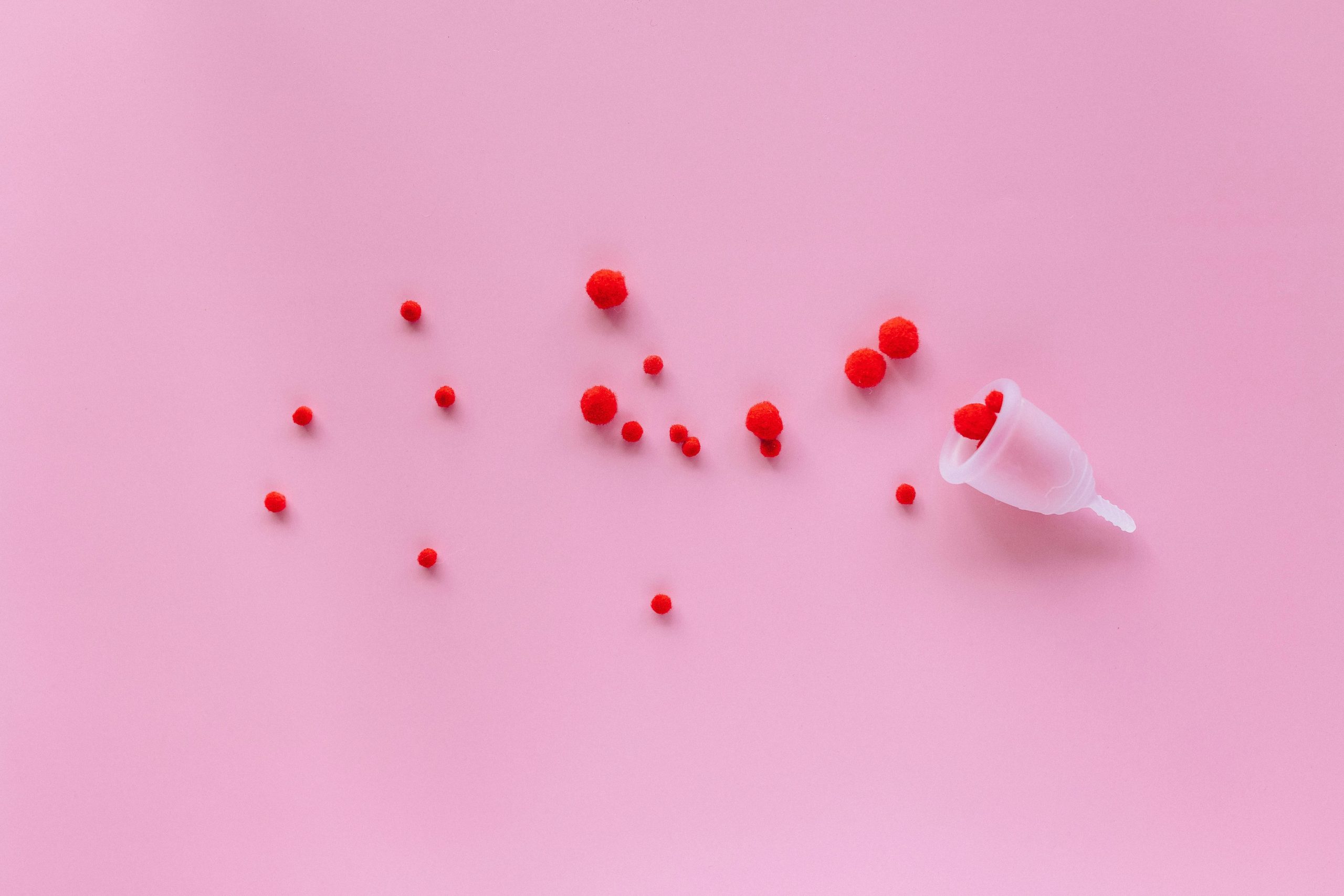 Menstrual cup with red elements on pink background symbolizing menstruation and femininity.